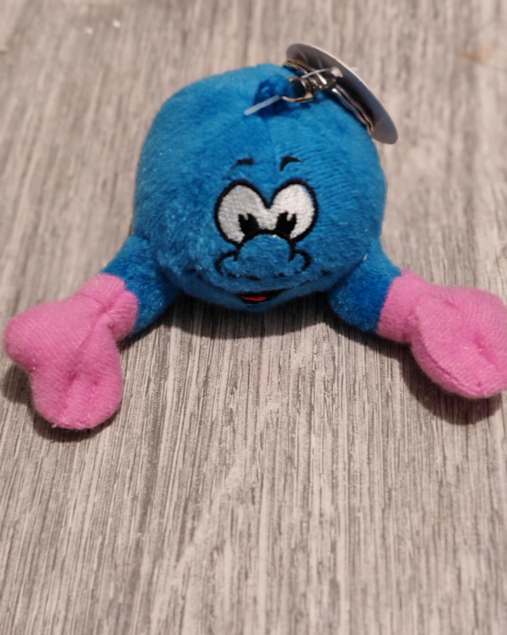 Blauwe pluche sleutelhanger met roze handjes en een lachend gezicht